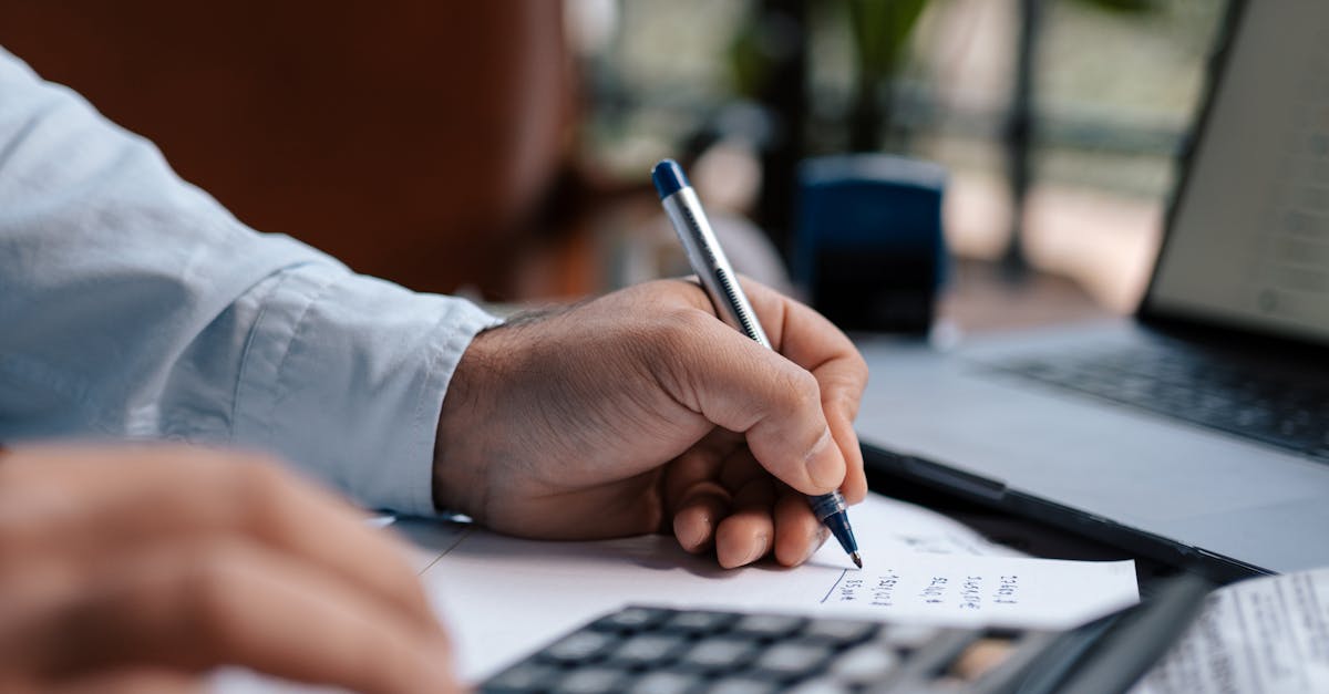 A person calculating finances with a calculator and pen on a desk indoors.