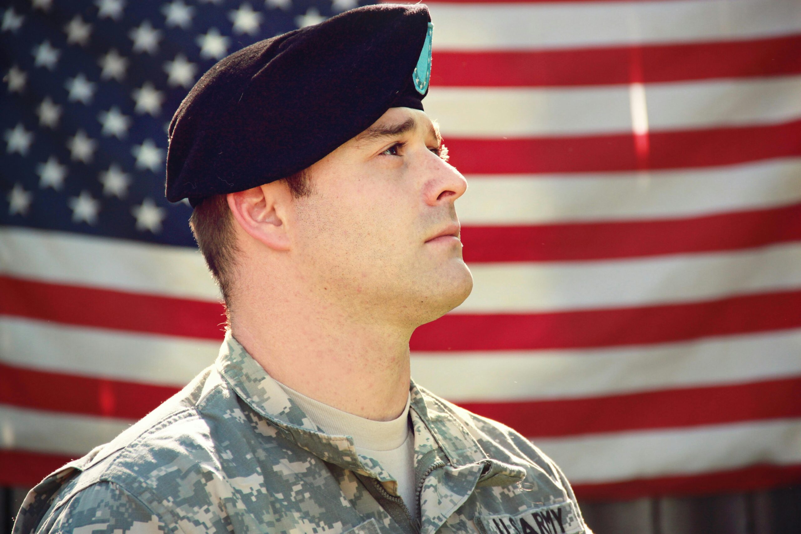 US soldier in uniform stands proudly with the American flag in the background, capturing a sense of patriotism.
