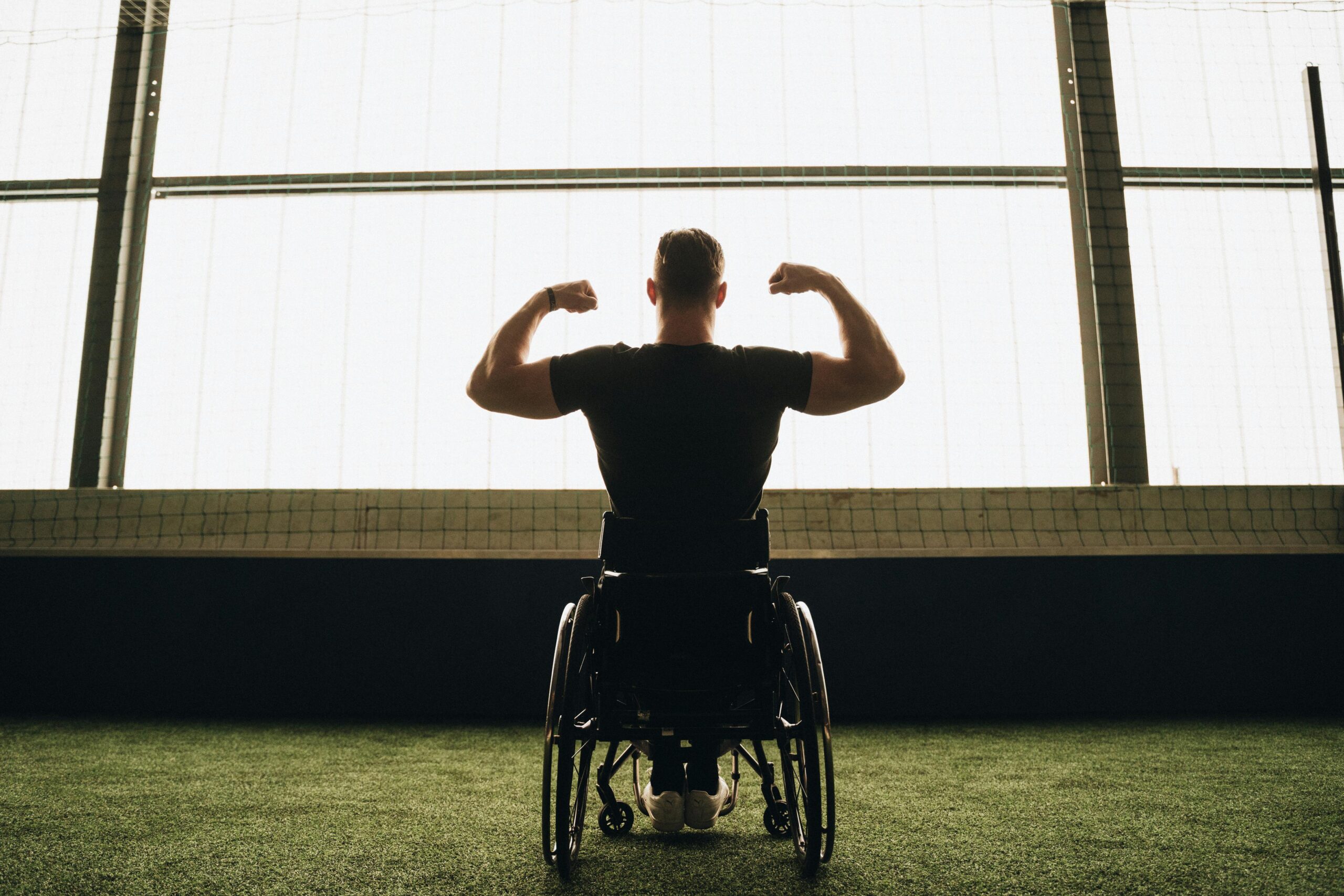Rear view of a muscular man in a wheelchair flexing in a sports facility.