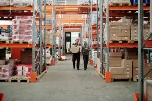 Two workers handle a package in a spacious warehouse surrounded by shelves stocked with boxes and products.
