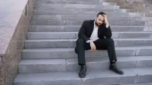 A businessman in a suit sits on stone steps, looking stressed and thoughtful outdoors.