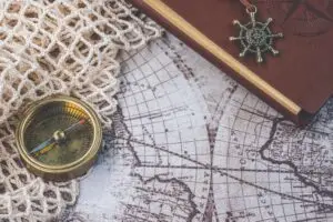 Flat lay of a vintage compass and leather notebook on a retro maritime map.
